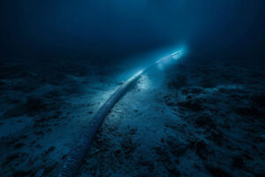 A wide-angle photograph capturing a fiber optic cable snaking across the ocean floor, illuminated by ambient light